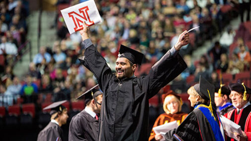 student in cap and gown holding up degree at UNL commencement 