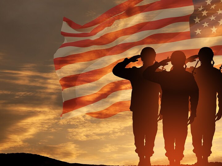 Military personnel in battle uniforms saluting American Flag